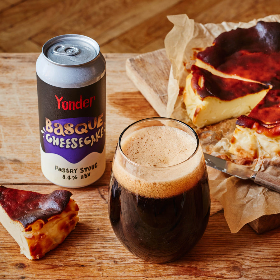 Basque cheesecake with a glass of dark beer and Yonder Basque Cheesecake can on a wooden board.
