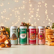 Load image into Gallery viewer, Four cans of Yonder beer with colorful labels on a table with pastries and blurred lights in the background
