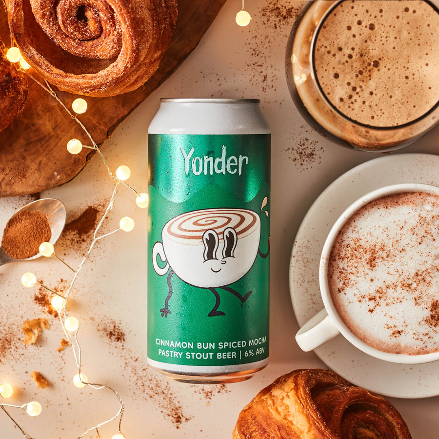 Yonder cinnamon bun spiced mocha beer can with a cup of coffee and cinnamon rolls on a light background.
