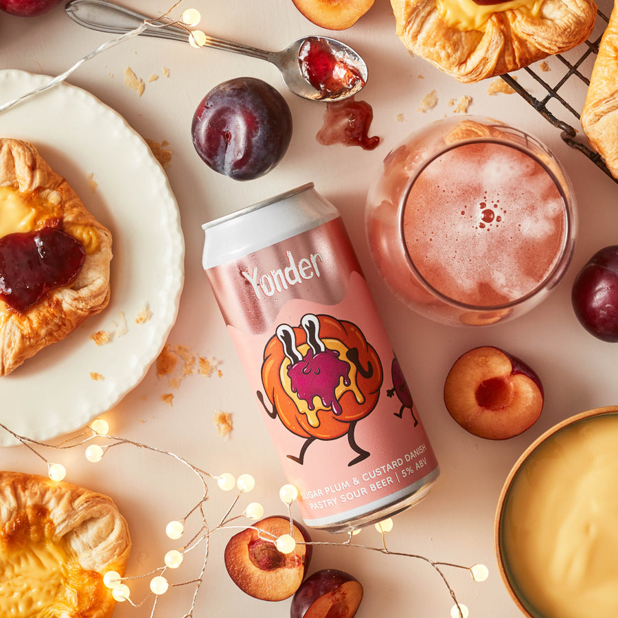 Yonder can with a plum-themed design, surrounded by pastries and fruit on a light background.